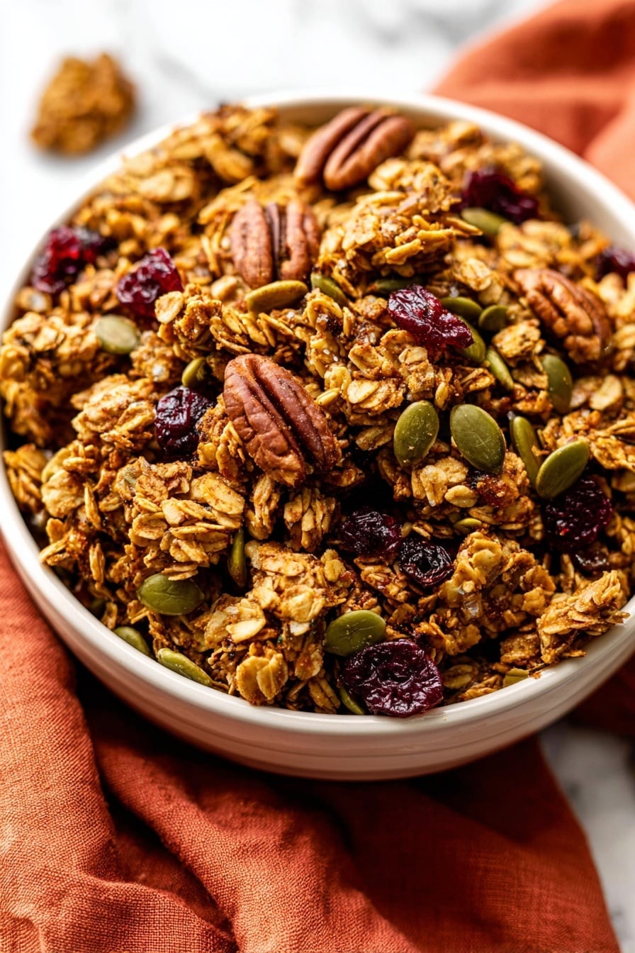 A close-up view of a white bowl filled with chunky granola clusters that have a golden-brown color and rough texture, mixed with whole pecans that are dark brown and ridged, green pumpkin seeds scattered throughout, and small pieces of deep red dried cranberries. The bowl is placed on top of a folded burnt orange cloth on a white marbled surface. photo taken with an iphone --ar 2:3 --v 7 - Pumpkin Spice Granola, fall granola recipe, cozy breakfast, crunchy pumpkin granola, healthy autumn snack