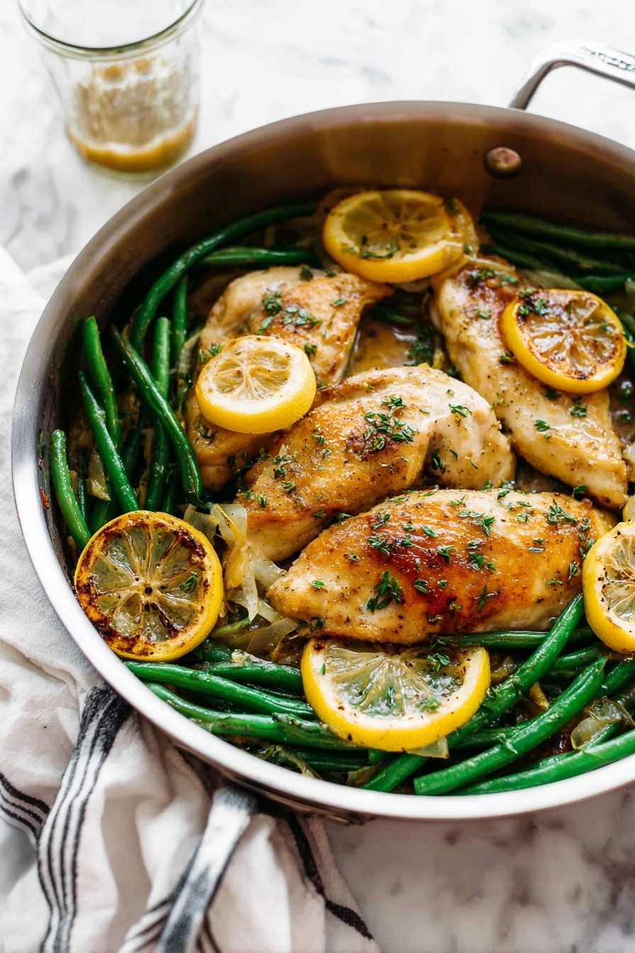 A round silver pan holds a dish with three light golden brown cooked chicken pieces on top. Underneath and around the chicken are bright green beans and several round slices of cooked lemon that are golden and slightly charred on the edges. The chicken is sprinkled with small green herb pieces and has a slightly shiny sauce coating parts of it. The pan is placed on a white marbled surface, with a white cloth with black stripes in the back left and a glass cup with some sauce behind the pan. Photo taken with an iphone --ar 2:3 --v 7 - Garlic Lemon Butter Chicken Skillet, easy chicken skillet recipe, one-pan chicken dinner, lemon garlic chicken, healthy chicken recipes
