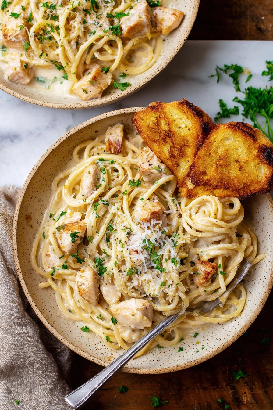 A close-up view of creamy pasta shows thick spaghetti strands coated in a smooth, light beige sauce. Mixed in are small chunks of grilled light brown chicken, with specks of black pepper and green parsley leaves scattered on top. A white piece of bread with a golden-brown crust rests on the side of the plate. A black fork is twirling some noodles and chicken. The plate has a rustic look with a speckled edge and sits on a white marbled surface. photo taken with an iphone --ar 2:3 --v 7 - Garlic Parmesan Chicken Pasta, creamy garlic pasta, easy chicken pasta, quick dinner recipe, cheesy chicken pasta