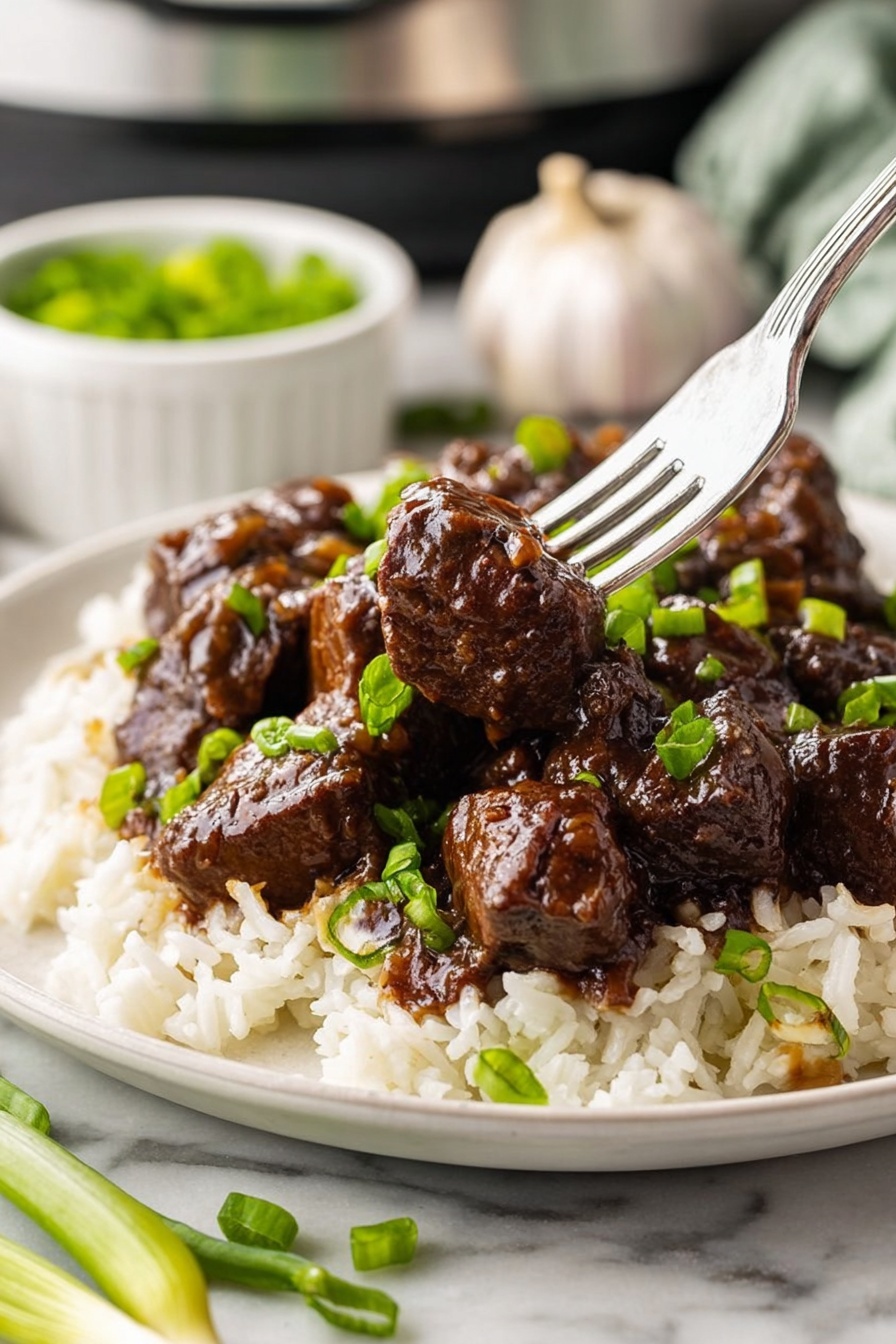 The dish shows a single white plate on a white marbled table, holding two main layers: the bottom layer is white rice with some chopped green onions scattered on top, and the top layer is dark brown beef chunks covered in a shiny glaze, also garnished with green onions. A silver fork pierces one beef chunk in the center of the plate, lifting it slightly above the rest. In the background, a whole garlic bulb and a small white bowl with more green onions are partially visible, adding to the kitchen setting. Photo taken with an iphone --ar 2:3 --v 7 - Honey Garlic Steak Bites, Honey Garlic Steak Bites recipe, easy steak bites, savory garlic steak, quick steak dinner