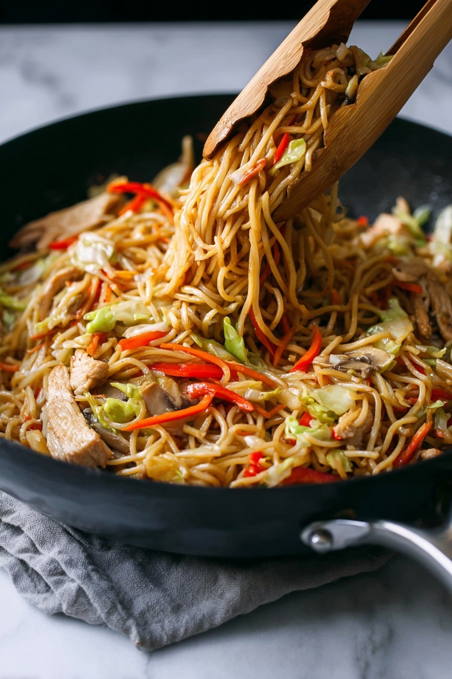 A close-up of a black skillet filled with cooked stir-fried noodles lifted by wooden tongs, showing three main layers: a base layer of thin, light brown noodles tangled together; mixed throughout are slices of light beige cooked meat and strips of vegetables including red bell peppers, pale green cabbage, thin orange carrot sticks, and light brown mushrooms. The noodles have a slightly shiny texture, and the colors of the vegetables add bright, fresh contrast. The skillet rests on a white marbled surface with a subtle grey cloth partially visible under the handle. photo taken with an iphone --ar 2:3 --v 7 - Chicken Yakisoba Stir-Fry, Japanese stir-fry recipes, easy chicken noodle stir-fry, quick Asian dinner ideas, simple yakisoba with chicken