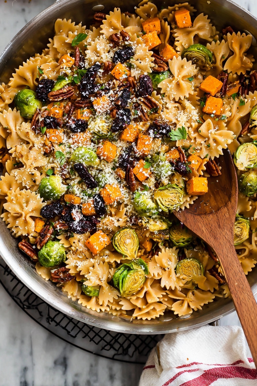 A large silver pan filled with a colorful pasta dish featuring three layers: the bottom layer has light brown farfalle pasta with smooth, slightly shiny texture; the middle layer contains bright orange small cubed roasted vegetables and sliced green brussels sprouts, some with charred marks, scattered evenly; the top layer is sprinkled with chopped dark brown pecans, black dried fruit pieces, small green herb leaves, and a light dusting of finely grated white cheese. A wooden spoon with a rounded bowl sits inside the pan. The pan rests on a black wire rack with a white cloth with red stripes on the side, all set on a white marbled surface. Photo taken with an iphone --ar 2:3 --v 7 - Brussels Sprouts Pasta with Brown Butter, Brussels Sprouts Pasta, Brown Butter Pasta, Fall Vegetable Pasta, Easy Brussels Sprouts Recipe