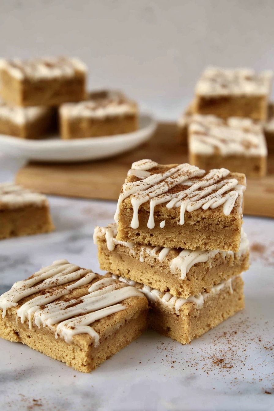 A stack of four square bars sits on a white marbled surface, each bar having a light golden brown color with a soft, crumbly texture. The bars are topped with lines of white icing dripping down the sides, and a sprinkling of fine brown powder. Nearby, a single bar lies flat, showing its thick layer and the decorated top. In the background, more bars with the same look rest on a white plate and a wooden board, all against a blurred white marbled texture background. photo taken with an iphone --ar 2:3 --v 7 - Cinnamon Sugar Blondies with Cinnamon Glaze, cinnamon blondie bars, easy cinnamon dessert, buttery cinnamon bars, cinnamon glaze blondies