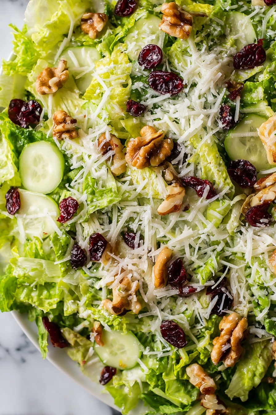 The image shows a close-up view of a fresh salad with several layers. The base layer consists of thinly shredded bright green lettuce. Scattered on top are thin slices of pale green cucumber, adding a smooth texture. There are pieces of light brown walnuts sprinkled across, giving a rough, chunky look. Interspersed are small dark red dried cranberries providing contrasting color and texture. The final layer is a light dusting of white shredded cheese spread evenly over the top. The salad is on a white plate placed over a white marbled surface. photo taken with an iphone --ar 2:3 --v 7 - Crispy Brussels Sprouts Salad with Apples, Brussels Sprouts apple salad, healthy Brussels Sprouts salad, easy Brussels Sprouts side dish, fruit and vegetable salad