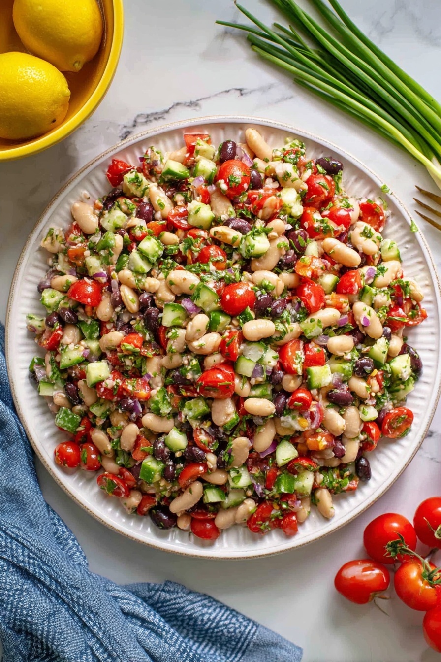 A white plate is filled with a colorful bean salad that has many small chopped pieces. The salad has white beans, red cherry tomato pieces, small green cucumber chunks, black beans, and bits of green herbs evenly spread on top. The texture looks fresh and slightly moist, mixed but not mushy. Around the plate, there are whole cherry tomatoes to the right, some green onions laying on a white marbled surface in the upper right, and a yellow bowl with lemons in the upper left. A blue cloth is partially visible under the plate. Photo taken with an iphone --ar 2:3 --v 7 - Mediterranean Bean Salad with Feta, healthy bean salad, quick Mediterranean salad, protein-packed vegetarian salad, easy feta bean salad