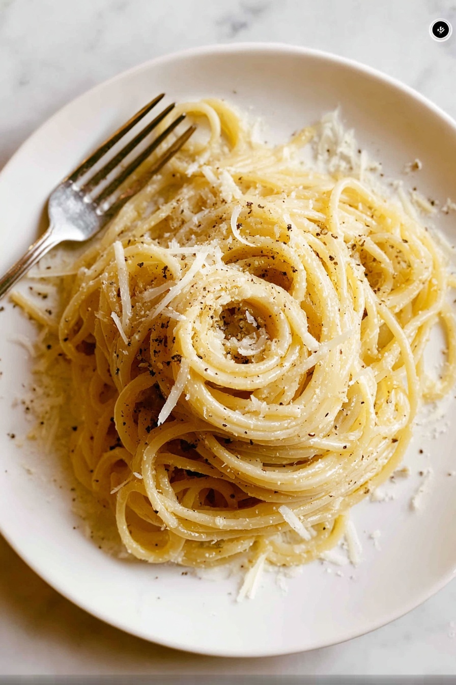 A white round plate holds a neatly twirled mound of spaghetti pasta as the main layer, pale yellow in color with a slight shine. Scattered over the pasta are small, irregular shreds of white cheese that add texture and light contrast to the smooth noodles. Black pepper flakes are sprinkled lightly, creating small dark spots across the dish. To the left side of the plate, a silver fork is partially visible, resting beside the pasta. The background has a white marbled texture, creating a clean and simple setting. Photo taken with an iphone --ar 2:3 --v 7 - Quick Cacio e Pepe with Bucatini, easy Cacio e Pepe pasta, creamy peppery pasta recipe, 15-minute Italian dinner, simple bucatini pasta