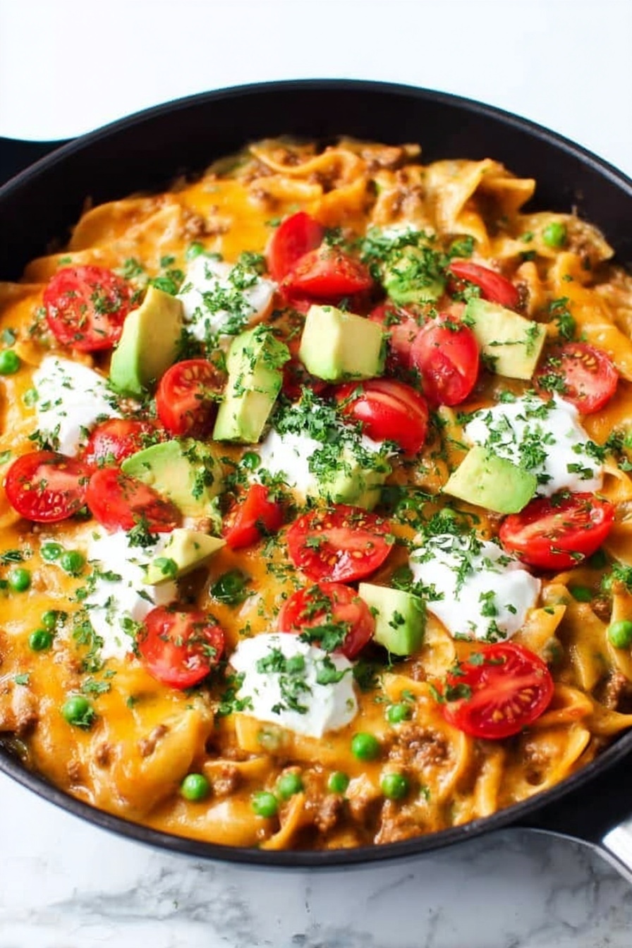 A black cast iron pan filled with a layered baked pasta dish topped with melted bright orange cheese, scattered green chopped herbs, and chopped green onions. On top are halved red cherry tomatoes, chunks of light green avocado, and dollops of white sour cream. A wooden spoon is scooping some of the pasta from the right side, showing short tube-shaped pasta mixed with meat and sauce underneath the cheese layer. The whole scene is set on a white marbled surface. photo taken with an iphone --ar 2:3 --v 7 - Cheesy Enchilada Pasta, enchilada pasta recipe, one-pot Tex-Mex pasta, cheesy pasta skillet, easy enchilada pasta
