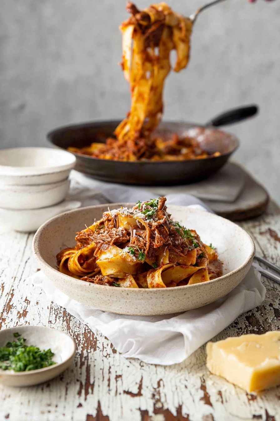 A white bowl with a rough texture holds several layers of wide flat pasta ribbons in a reddish-brown tomato sauce mixed with shredded meat, topped with green parsley and a sprinkle of grated cheese. Behind it, a dark pan contains more pasta in sauce being lifted upwards, while an empty white bowl rests on a white cloth on a worn white marbled table with chipped paint. To the left of the bowl is a small dish of chopped green herbs, and at the bottom right a grater with a chunk of yellow cheese sits on the table. The scene is light and rustic, photo taken with an iphone --ar 2:3 --v 7 - Slow Cooker Beef Ragu Pasta, Beef Ragu, Slow Cooker Recipes, Comforting Pasta Dishes, Easy Beef Pasta