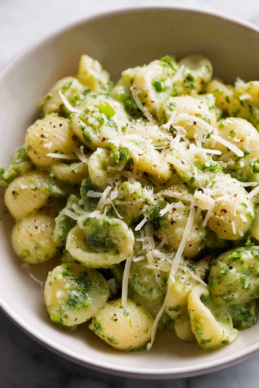 A large bowl filled with small spiral pasta mixed with bright green broccoli florets. The pasta is light yellow and looks soft, while the broccoli pieces are spread evenly throughout the dish. On top, there is a sprinkling of grated parmesan cheese, adding a slight white textured layer. A silver spoon is placed inside the bowl on the left side, ready to serve. In the background, there are two stacked white bowls, a silver fork and spoon set on a white cloth, and a block of parmesan cheese next to a grater on a white marbled surface. The overall setting feels cozy and inviting. photo taken with an iphone --ar 2:3 --v 7 - Quick Broccoli Pasta with Lemon and Cheese, healthy broccoli pasta, easy lemon pasta recipe, quick weeknight dinner ideas, cheesy garlic pasta