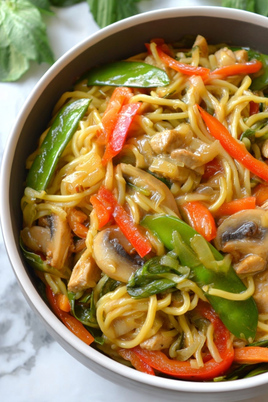 The image shows a close-up of a bowl filled with a colorful noodle stir-fry. The bottom layer consists of long, light yellow noodles, mixed evenly with sliced vegetables including bright green snow peas, orange thin carrot strips, chunky red bell pepper pieces, and light brown mushroom slices. There are also pieces of light tan tofu or chicken mixed into the dish. The noodles and vegetables are coated with a glossy sauce, giving them a shiny and slightly wet texture. The bowl is white, and it sits on a white marbled surface with some green leaves blurred in the background. photo taken with an iphone --ar 2:3 --v 7 - Instant Pot Chicken Lo Mein, Chinese chicken noodle stir-fry, quick weeknight dinner, healthy Instant Pot recipes, easy Asian inspired meal