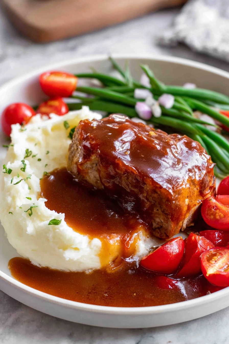 A white plate shows a thick layer of smooth white mashed potatoes on the left side, topped with a glossy brown sauce that pools around the dish. On top of the potatoes sits a piece of cooked meat covered in the same brown sauce, with a slice cut to reveal the inside texture. Behind the meat, there is a row of green beans and bright red cherry tomato halves scattered around, garnished with small pieces of chopped onions. The plate rests on a white marbled surface. Photo taken with an iphone --ar 2:3 --v 7 - Oven Baked BBQ Chicken with Homemade Sauce, easy baked BBQ chicken, homemade BBQ sauce recipe, juicy baked chicken thighs, simple oven chicken recipes