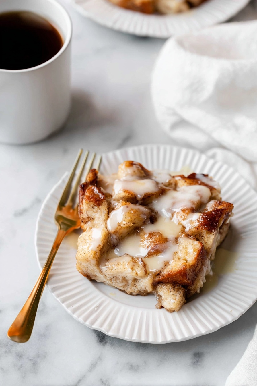 A piece of bread pudding with chunky, soft golden pieces of baked bread layered unevenly, soaked in a creamy, slightly shiny white sauce drizzled on top. The bread looks light brown with some darker toasted edges, sitting on a white plate with a subtle scalloped edge. A gold fork is placed on the left side of the plate. The plate rests on a white marbled surface, and a soft white cloth is partially visible in the upper right corner. There is also a white cup filled with dark coffee in the top left corner. photo taken with an iphone --ar 2:3 --v 7 - Apple Pie Cinnamon Roll Bake, fall breakfast recipes, easy cinnamon roll bake, apple dessert casseroles, cozy brunch ideas