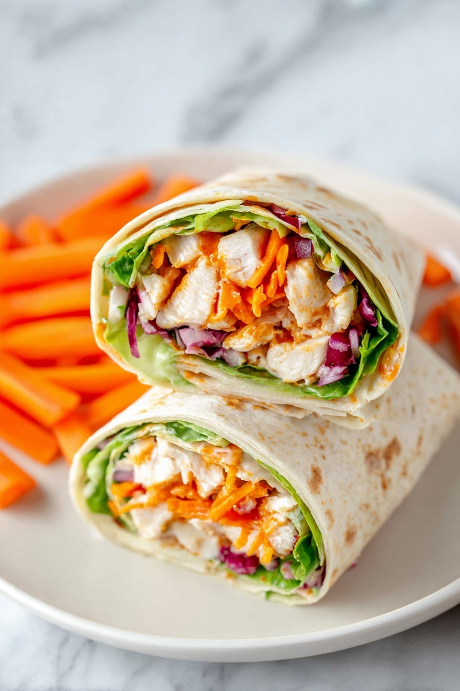 Two wrap halves are placed side by side on a white plate with small orange carrot sticks scattered around. Each wrap shows clear layers starting with a light tortilla on the outside, next a layer of fresh green lettuce, followed by chunks of white chicken mixed with orange sauce, bright orange shredded carrots, and pieces of red onion. The wraps are cut cleanly, exposing the colorful and fresh filling inside. The plate is set on a white marbled surface. Photo taken with an iphone --ar 2:3 --v 7 - Buffalo Chicken Wraps, Buffalo Chicken Wraps recipe, easy buffalo chicken wraps, spicy chicken wrap, quick lunch wraps