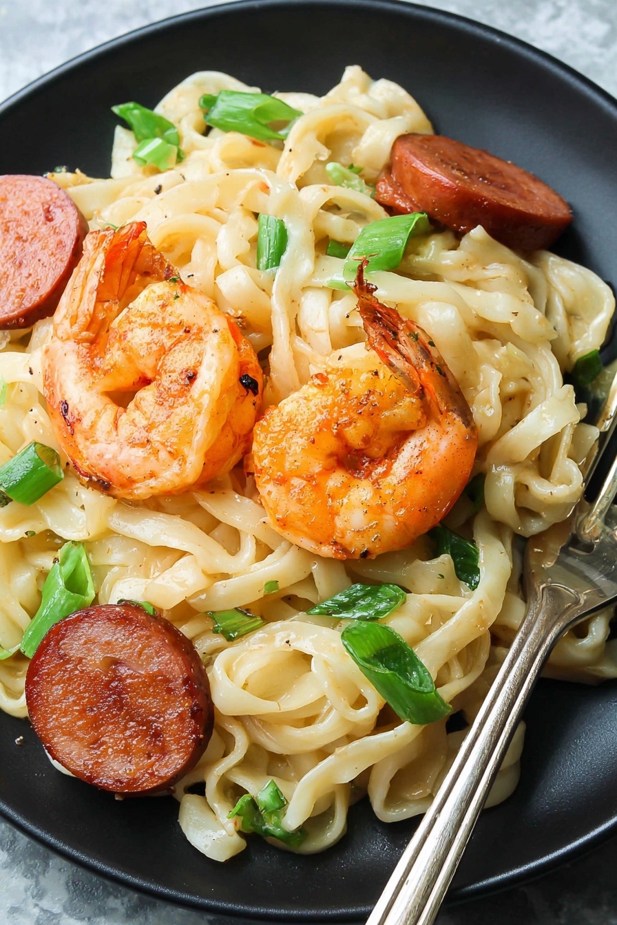 The dish shows a close-up view of a black pan filled with several layers of food, starting from a base of creamy beige flat noodles tangled together, mixed with orange-pink cooked shrimp scattered on top and throughout. There are dark red-brown sausage slices peeking through, along with chunks of light green celery and small pieces of bright green onion adding color contrast. Small black pepper specks are spread over the noodles and shrimp, giving the dish a light seasoning look. A metal utensil lifts some of the noodles from the pan's side. The background is a white marbled texture. Photo taken with an iphone --ar 2:3 --v 7 - Cajun Shrimp and Sausage Pasta, Cajun Shrimp Pasta, Spicy Cajun Pasta, Creamy Shrimp and Sausage Pasta, Easy Cajun Pasta
