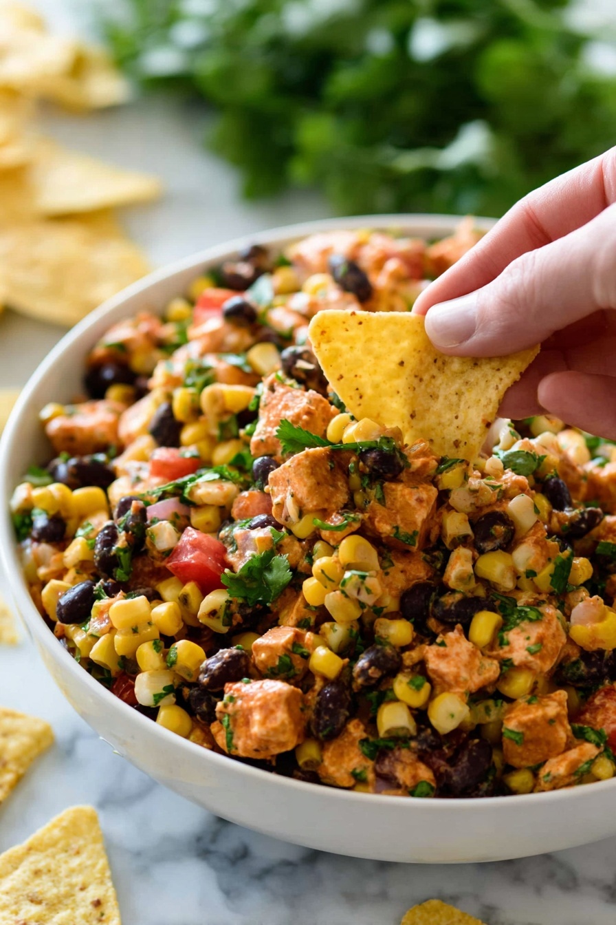 A white bowl is filled with a mixed salad containing small, yellow corn kernels, black beans, orange-colored diced pieces that look like chicken or tofu, and small bits of green herbs scattered on top. There are also small cubes of red tomato or bell pepper mixed in. A woman's hand is holding a pale yellow triangular tortilla chip, scooping some of the salad from the bowl. The background is a white marbled surface, and some green leafy vegetables can be seen blurred in the back along with a few tortilla chips scattered around the bowl. Photo taken with an iphone --ar 2:3 --v 7 - Southwest Chicken Salad with Black Beans, Southwest Chicken Salad, Black Bean Chicken Salad, Healthy Southwest Chicken Salad, Easy Southwest Salad