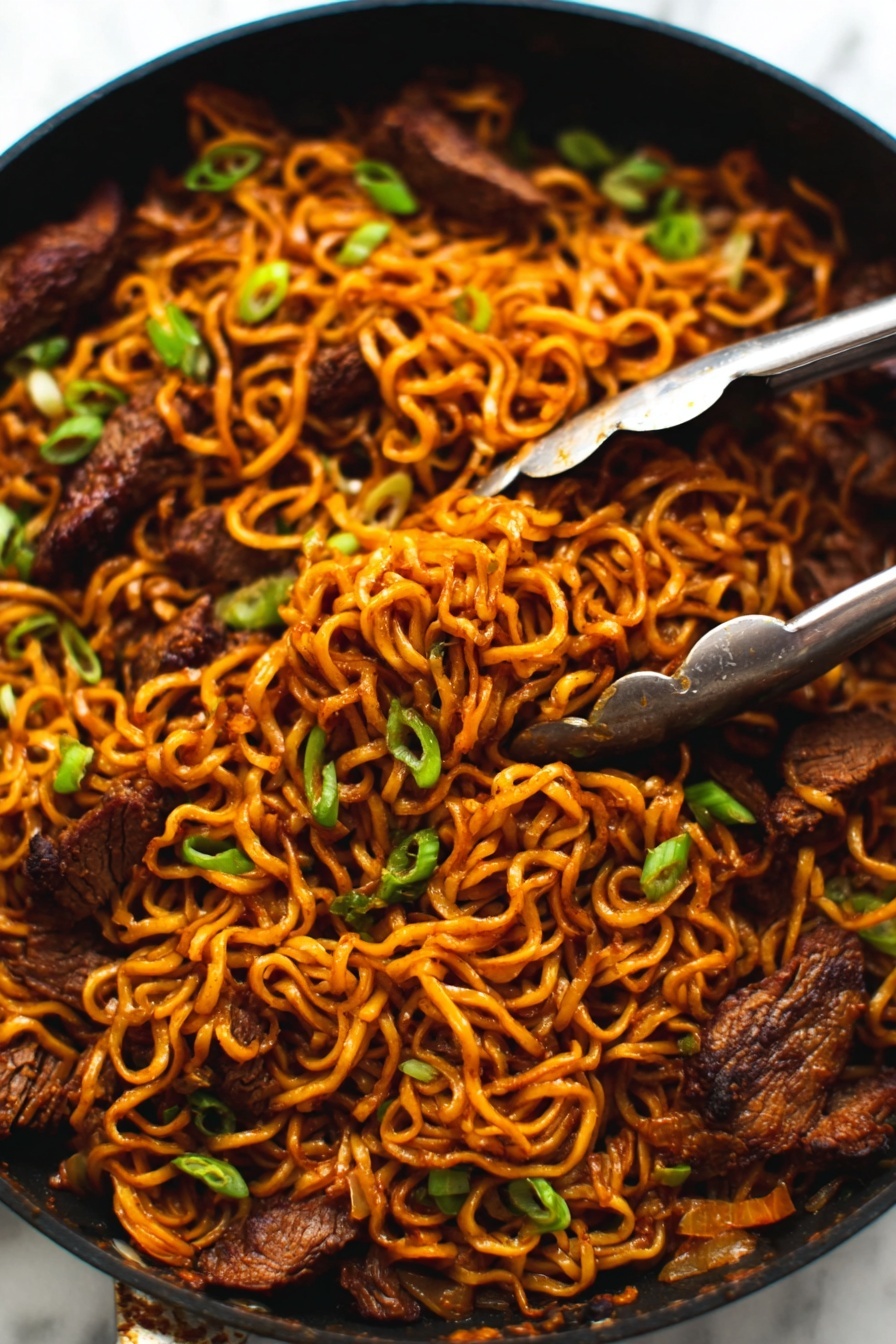 The image shows a close-up of a black pan filled with cooked noodles mixed with pieces of dark brown meat. The noodles are a warm orange-brown color, twisted and tangled together with small green onions sprinkled on top for color contrast. A pair of silver tongs is gripping some noodles and meat in the top right area of the pan. The pan sits on a white marbled surface. photo taken with an iphone --ar 2:3 --v 7 - Spicy Korean Beef Noodles, Korean beef noodle stir-fry, spicy Korean ramen, Korean beef marinade recipe, quick Korean noodle dish