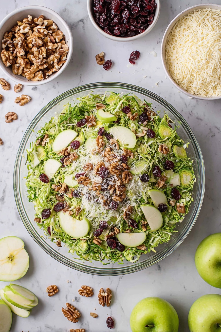 A large clear glass bowl filled with a fresh salad showing three layers: the bottom layer is shredded green Brussels sprouts, the middle layer is thinly sliced green apple slices placed evenly around, and the top layer is scattered walnut pieces, dark red dried cranberries, and small white grated cheese bits, all on a white marbled surface. Around the bowl are small white bowls containing walnuts, grated cheese, and dried cranberries, along with whole and sliced green apples and loose salad leaves scattered nearby. Photo taken with an iphone --ar 2:3 --v 7 - Crispy Brussels Sprouts Salad with Apples, Brussels Sprouts apple salad, healthy Brussels Sprouts salad, easy Brussels Sprouts side dish, fruit and vegetable salad