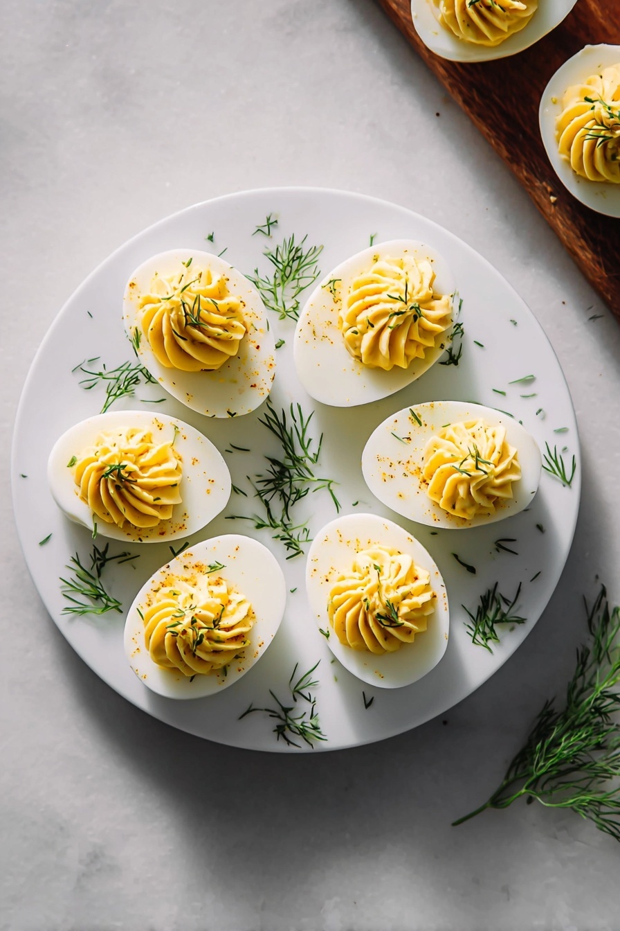 The image shows a white round plate on a white marbled surface. On the plate, there are six deviled egg halves arranged in a circle. Each deviled egg has a smooth white egg white base and a creamy, swirled yellow yolk filling on top, garnished with small green dill pieces sprinkled over and around the eggs. To the right side of the plate, there are three more deviled eggs partially visible on the same white marbled surface. Bright, natural light highlights the smooth textures and fresh garnishes, giving the dish a clean and appetizing look. Photo taken with an iphone --ar 2:3 --v 7 - Creamy Classic Deviled Eggs, deviled eggs recipe, easy party appetizers, creamy deviled eggs, classic egg salad appetizers