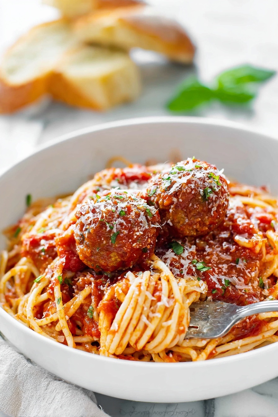 A large red pot holds a mix of spaghetti and meatballs in a rich tomato sauce. The spaghetti is long and golden, twisted around and soaked in the chunky red sauce. The meatballs are round and brown, scattered evenly through the noodles, some partially covered with sauce. A wooden spoon with a smooth light wood texture is stirring the pasta, with some sauce on it. The pot’s inside edge shows a coating of the thick tomato sauce. The background has a white marbled texture. photo taken with an iphone --ar 2:3 --v 7 - Homemade Spaghetti and Meatballs, Italian spaghetti and meatballs, classic spaghetti with meatballs, homemade marinara sauce, easy Italian dinner