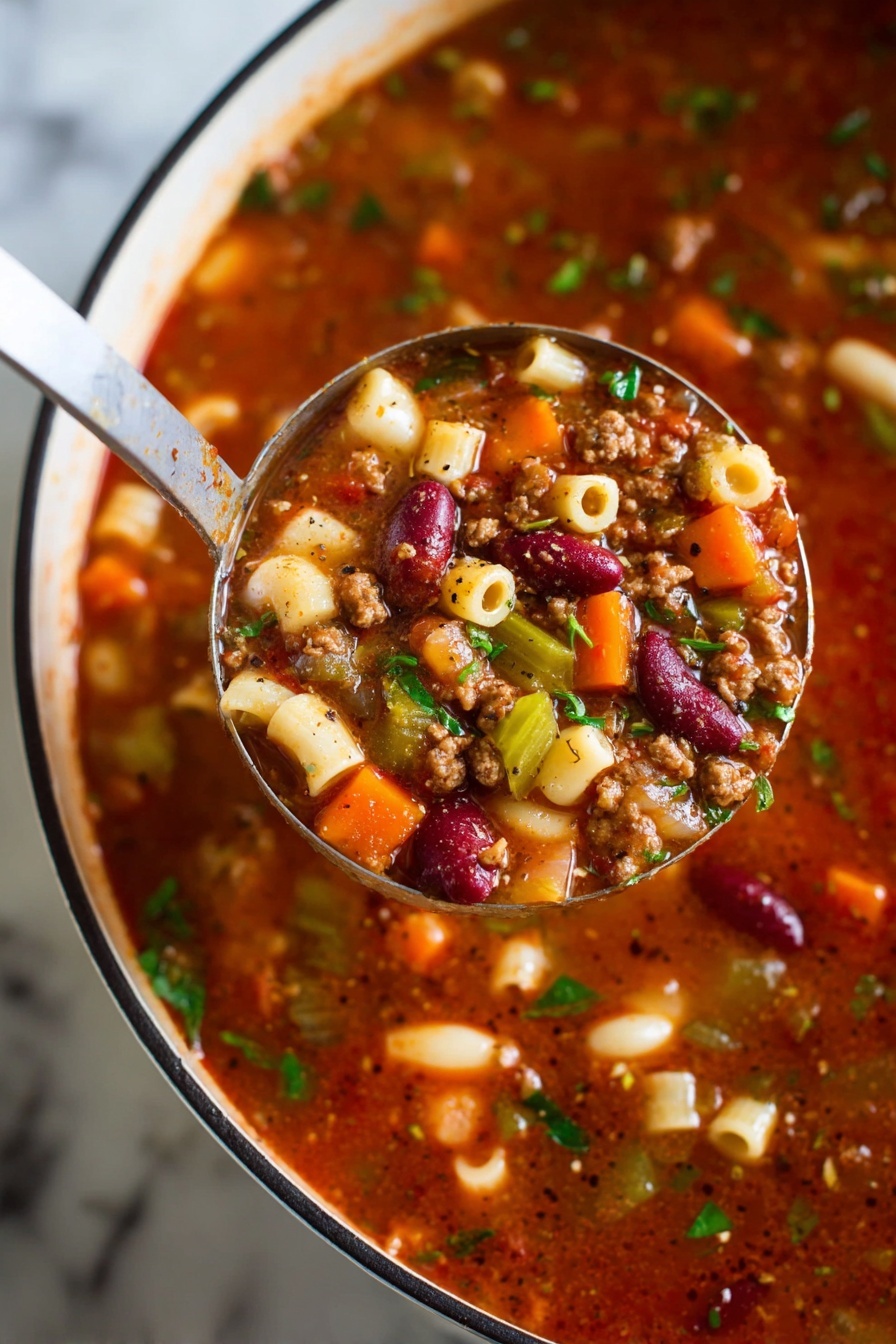 A close-up view of a ladle holding a rich, chunky soup above a white pot with a black rim, all resting on a white marbled surface. The soup has multiple layers visible: a thick, deep red broth base mixed with small bits of brown ground meat, bright orange carrot cubes, pale white and red kidney beans, green celery slices, and small round pasta pieces. Fresh green herbs are sprinkled throughout, adding a fresh touch. Black pepper flecks are visible on the surface of the soup and ladle, giving it a seasoned look. photo taken with an iphone --ar 2:3 --v 7 - Creamy Pasta e Fagioli Soup, Italian pasta and bean soup, hearty Italian bean soup, easy Pasta e Fagioli recipe, comforting Italian soup