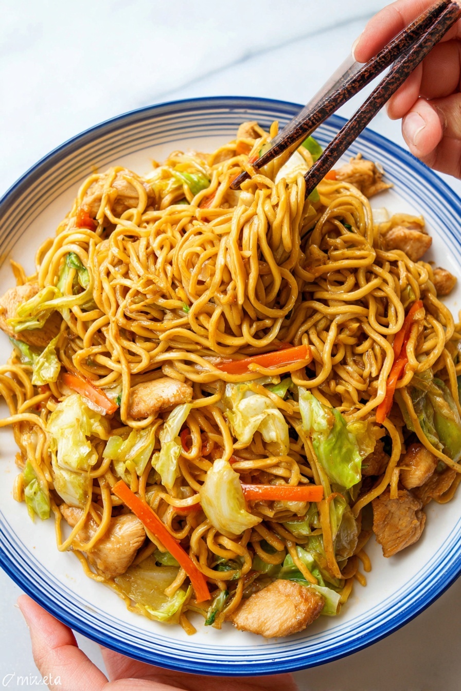 A white plate with a blue rim holds a serving of stir-fried noodles mixed with pieces of cooked light brown chicken, bright orange carrot sticks, and green cabbage leaves. The noodles are golden yellow and tangled together, with some lifted by dark brown chopsticks held by a woman's hand above the plate. The plate is on a white marbled surface, and the woman’s hand is seen at the bottom left corner holding the plate slightly. Photo taken with an iphone --ar 2:3 --v 7 - Easy Chicken Yakisoba Stir-Fry, chicken yakisoba recipe, easy stir-fry dinner, quick Japanese noodles, simple chicken stir-fry