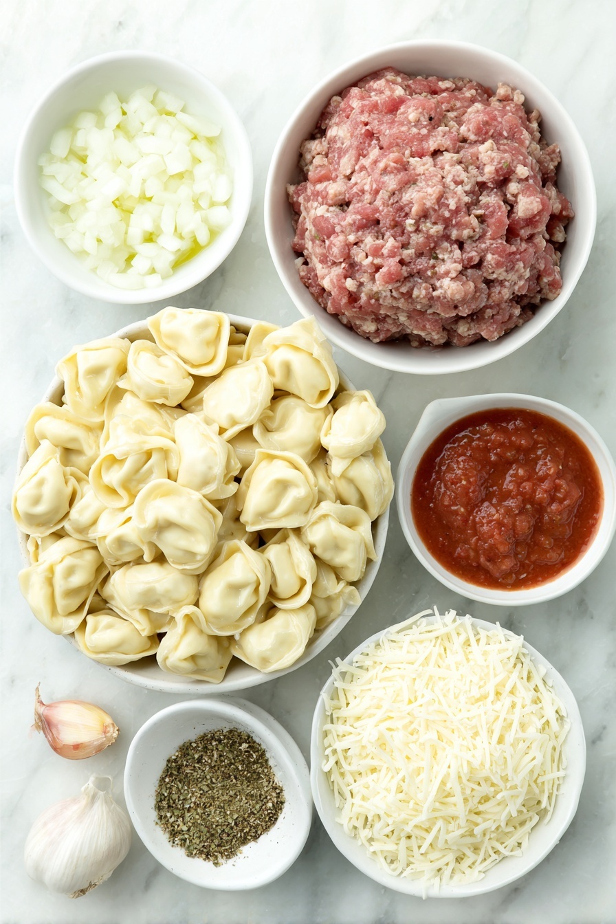 Flat lay of a mound of fresh cheese tortellini, a small white ceramic bowl of golden olive oil, a white ceramic bowl holding three whole uncracked brown garlic cloves, a small pile of finely diced white onion, a portion of raw lean ground beef shaped neatly, a white ceramic bowl filled with bright red crushed tomatoes, another white ceramic bowl with smooth red tomato sauce, a small heap of dried Italian seasoning herbs, coarse kosher salt crystals scattered lightly, a few twists of freshly ground black pepper, and a small white ceramic bowl heaped with freshly grated mozzarella cheese, all arranged in perfect symmetry on a clean white marble surface, soft natural light, photo taken with an iPhone, professional food photography style, fresh ingredients, white ceramic bowls, no bottles, no duplicates, no utensils, no packaging --ar 2:3 --v 7 --p m7354615311229779997 - Cheesy Baked Tortellini Casserole, cheesy tortellini casserole, baked tortellini recipes, comforting pasta dishes, easy baked pasta