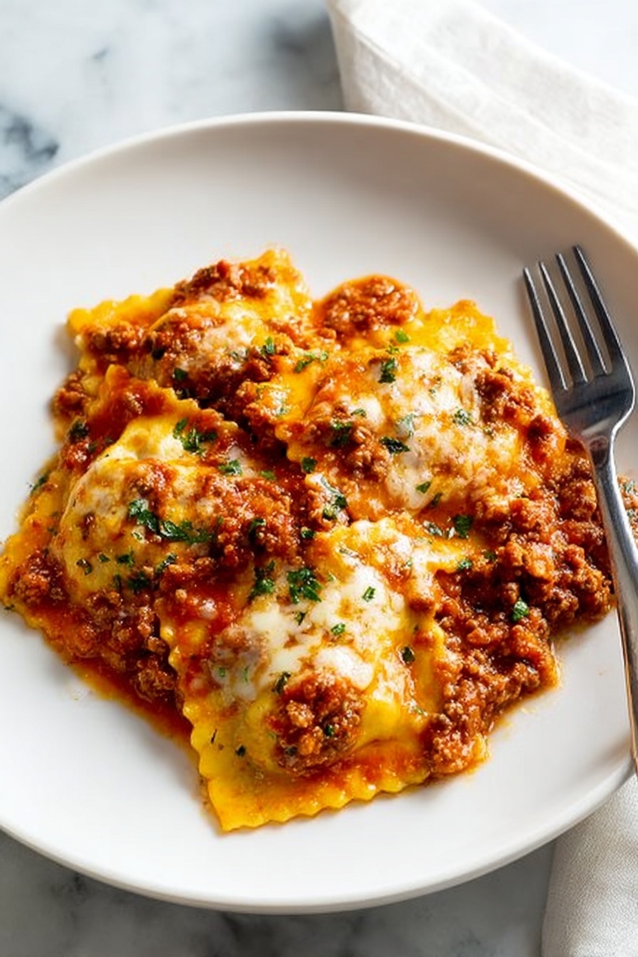 The dish shows four large square ravioli pieces covered in a thick, chunky tomato meat sauce with visible bits of ground meat and small green herb sprinkles on top. The ravioli have ruffled edges and are coated in melted cheese that is golden-yellow and slightly browned in spots. The sauce spreads evenly over the pasta, giving it a rich and hearty look. The white plate sits on a white marbled surface, with a fork resting on the right side of the plate. The lighting highlights the textures and colors, making the dish look warm and appetizing. photo taken with an iphone --ar 2:3 --v 7 - Cheesy Baked Ravioli with Meat Sauce, baked ravioli recipe, cheesy ravioli casserole, easy baked ravioli, hearty pasta bake