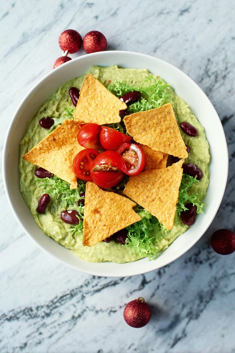 A white bowl filled with a creamy green guacamole base topped by several crispy golden tortilla chips placed in the center. Around the chips, there are bright red cherry tomato halves, fresh green lettuce leaves, and small dark red kidney beans scattered. The bowl is set on a white marbled surface. photo taken with an iphone --ar 2:3 --v 7 - Festive Guacamole with Pomegranate & Tomatoes, holiday avocado dip, quick holiday appetizers, colorful party dip, easy festive guacamole