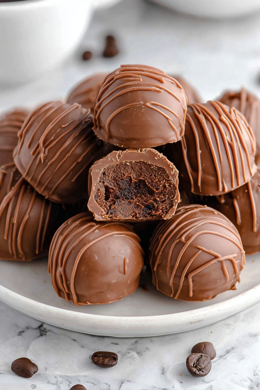 A white plate filled with round milk chocolate truffles, each truffle covered with thin milk chocolate drizzle lines on top. One truffle is broken in half and placed on top of the others, showing a thick, darker chocolate center with a smooth and slightly crumbly texture inside. The plate is on a white marbled surface with a few dark brown coffee beans scattered around. Photo taken with an iphone --ar 2:3 --v 7 - Coffee Chocolate Truffles, Coffee Chocolate Dessert Recipe, Handmade Coffee Chocolates, Easy No-Bake Truffle Recipe, Gourmet Coffee Chocolate Treats