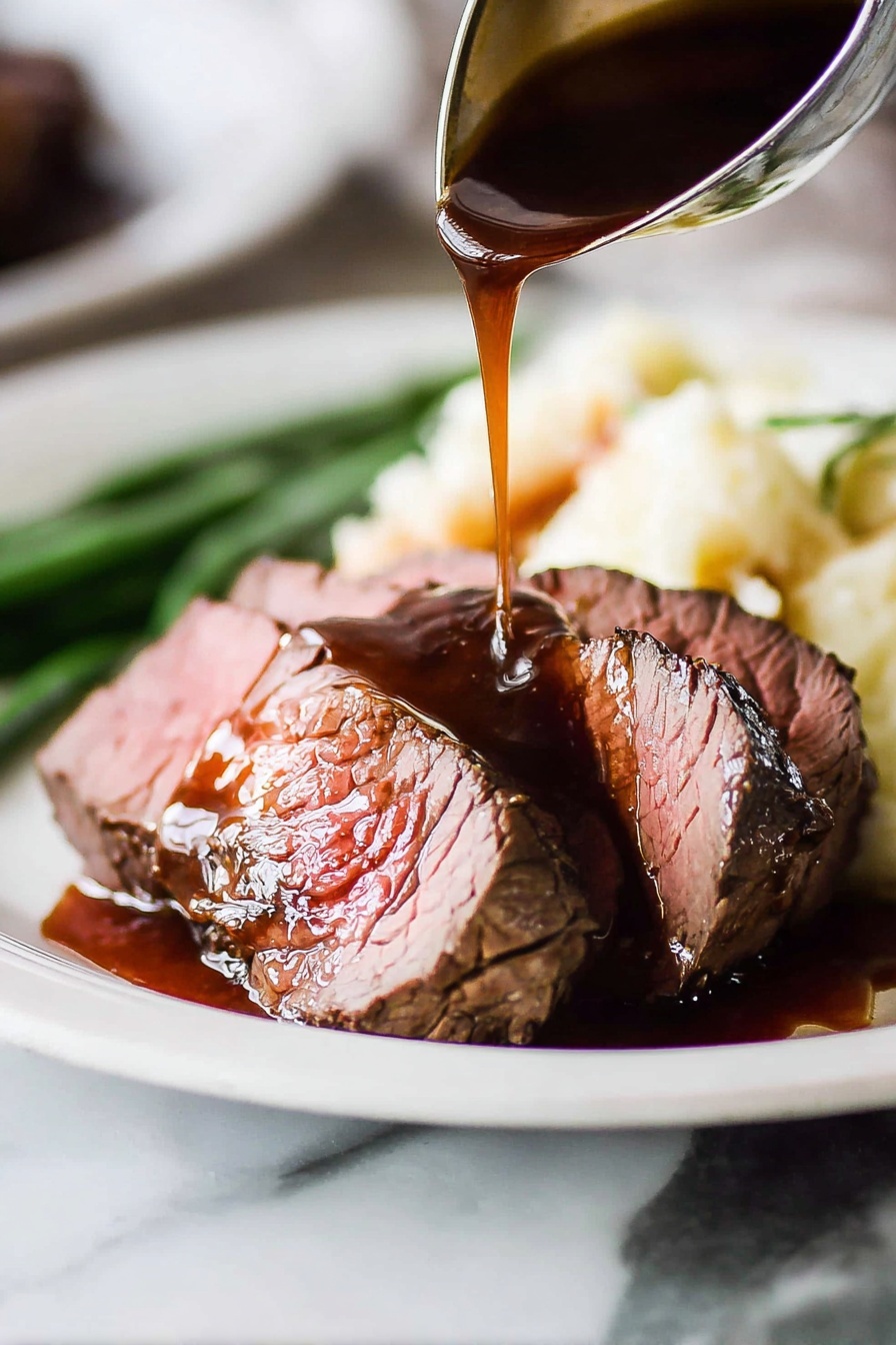 The image shows two thick slices of medium-rare roast beef placed on a white plate with a white marbled surface in the background. The roast beef has a brown crust on the outside and a pink center. A dark brown gravy sauce is being poured over the top slice from a ladle, creating a shiny texture with some sauce pooling on the plate. Behind the beef, there is a serving of creamy mashed potatoes and a few green beans slightly blurred in the background. The focus is on the meat and sauce with a close-up view emphasizing the moist texture of the beef and the rich shine of the gravy. Photo taken with an iphone --ar 2:3 --v 7 - Beef Tenderloin with Red Wine Sauce, elegant beef tenderloin recipe, easy red wine sauce for steak, fancy beef main dish, gourmet beef dinner