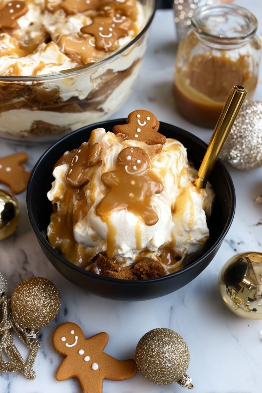 A black bowl filled with a layered dessert featuring white cream or marshmallow at the top, drizzled with light brown caramel sauce, and topped with small gingerbread man cookies that have a light brown color and smiling faces. The dessert shows a darker brown crumbly layer near the bottom contrasting with the creamy top. The bowl is placed on a white marbled surface, surrounded by more gingerbread cookies shaped like men and bells, along with two sparkly gold ornaments and a small jar of caramel sauce beside the bowl. A gold spoon rests inside the bowl, slightly submerged in the dessert. In the background, a glass bowl holds more of the same layered dessert. Photo taken with an iphone --ar 2:3 --v 7 - Gingerbread Trifle, Gingerbread Trifle Recipe, Holiday Trifle Dessert, Festive Gingerbread Layered Dessert, Easy Christmas Trifle