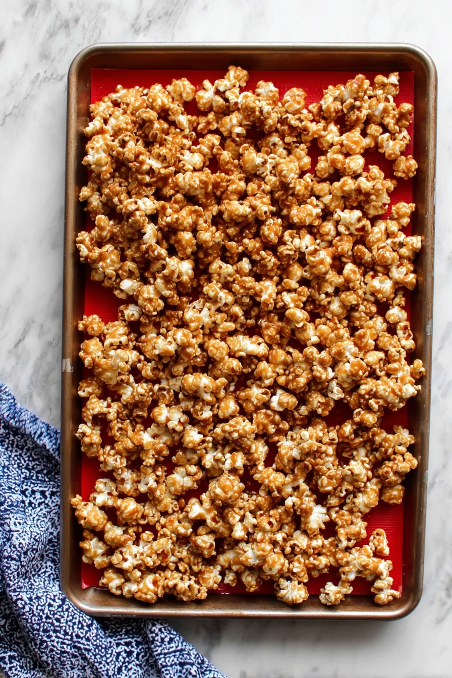 A rectangular white tin box filled with a single thick layer of caramel popcorn, where each popcorn piece is coated unevenly with a shiny golden-brown caramel glaze, showing some light and darker caramel spots. The popcorn looks puffy and slightly sticky, packed tightly inside the box which is lined with white parchment paper that curls over the sides. The box is placed on a surface with a white marbled texture. photo taken with an iphone --ar 2:3 --v 7 - Homemade Caramel Popcorn, caramel popcorn recipe, crunchy caramel popcorn, easy homemade popcorn, sweet buttery snack