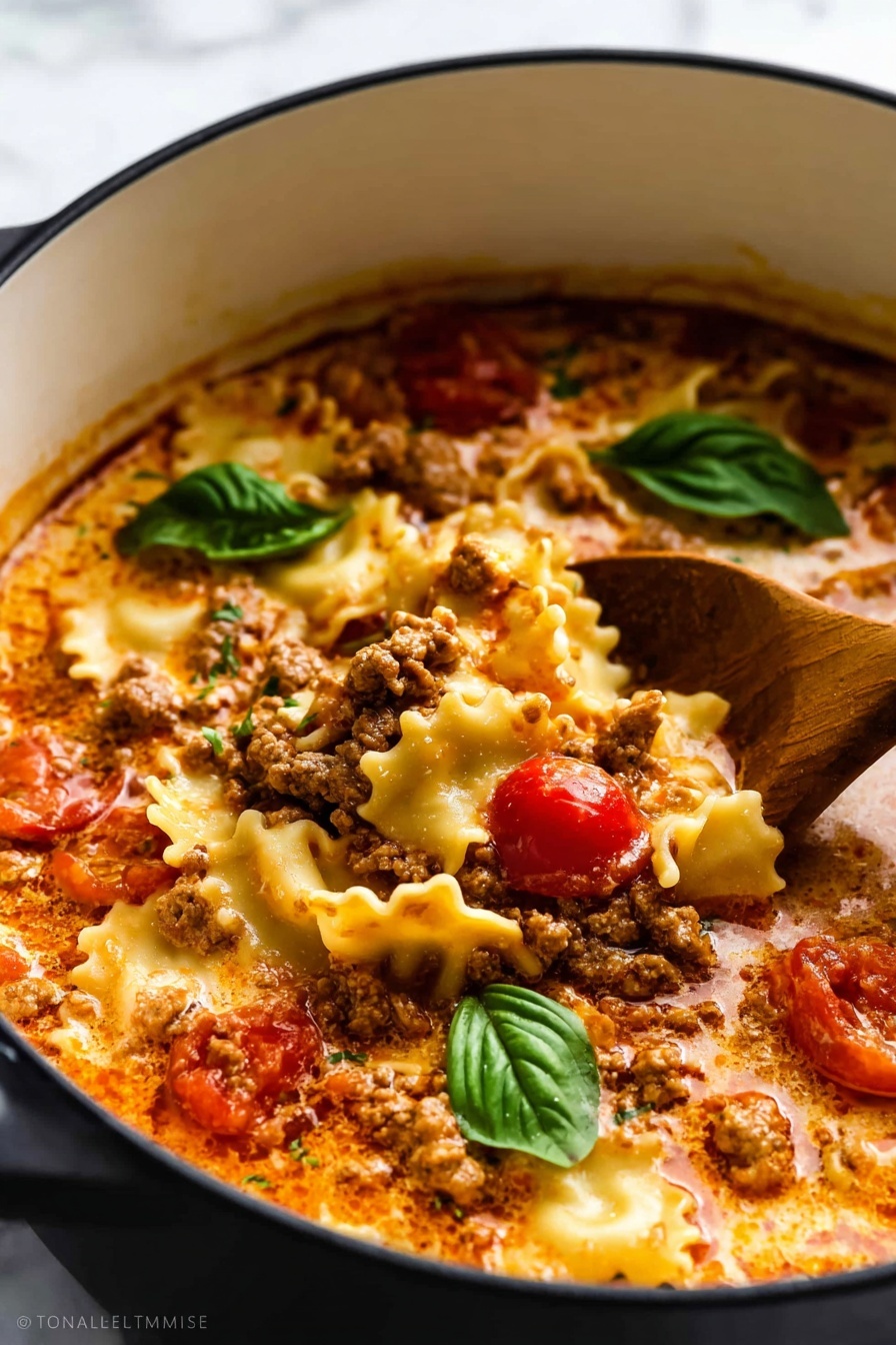 This image shows a close-up of a pot filled with a creamy lasagna soup. The dish has three main layers: the bottom layer is a rich tomato broth with creamy swirls, the middle layer has crumbled cooked ground meat with a brown color and a slightly crumbly texture, and the top layer includes wavy lasagna pasta pieces in a pale yellow color that float on the surface. There are whole cherry tomato pieces adding splashes of bright red throughout the soup. On top of the pasta and meat mixture sit a few fresh, green basil leaves, giving a fresh contrast to the warm colors. A wooden spoon dips into the soup from the side, stirring the ingredients gently. The pot is white with a black interior, sitting on a white marbled surface. photo taken with an iphone --ar 2:3 --v 7 - Lasagna Soup with Creamy Basil Ricotta, lasagna soup recipe, quick lasagna soup, healthy lasagna soup, creamy ricotta lasagna soup