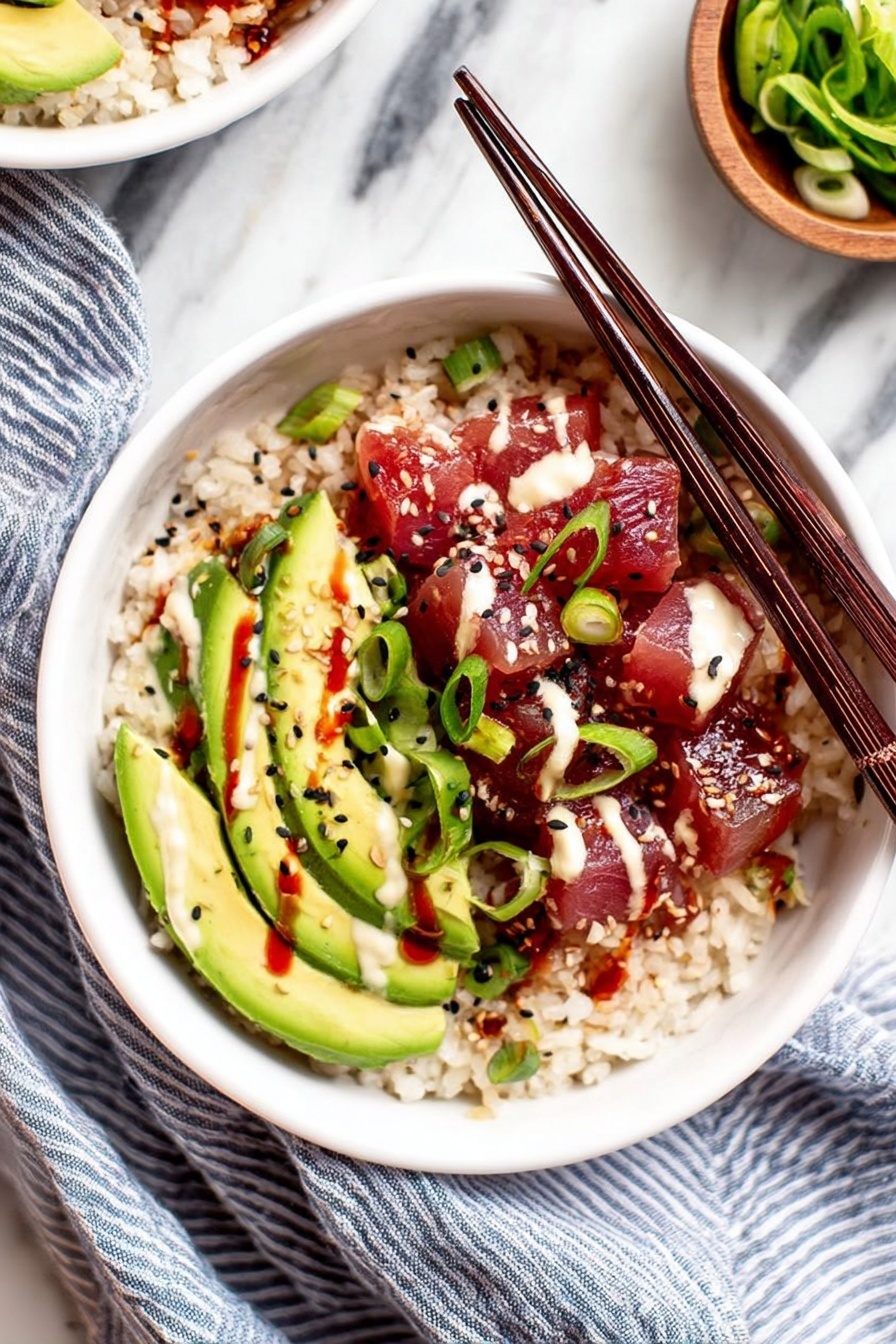 A white bowl filled with three main layers: the bottom layer is light brown cooked rice, the middle layer shows bright green avocado slices arranged in a fan shape on one side, and the top layer is deep red cubed raw fish covered with light cream sauce and red sauce drizzles. Small black sesame seeds and sliced green onions are scattered over the avocado and fish. Two dark wooden chopsticks rest diagonally across the bowl on top of the food. The bowl is placed on a white marbled surface with a blue striped cloth beside it, and a small wooden bowl with green sliced vegetables is partially visible in the background. Photo taken with an iphone --ar 2:3 --v 7 - Spicy Tuna Poke Bowl, tuna poke bowl, healthy poke bowl recipe, quick sushi bowl, spicy tuna salad