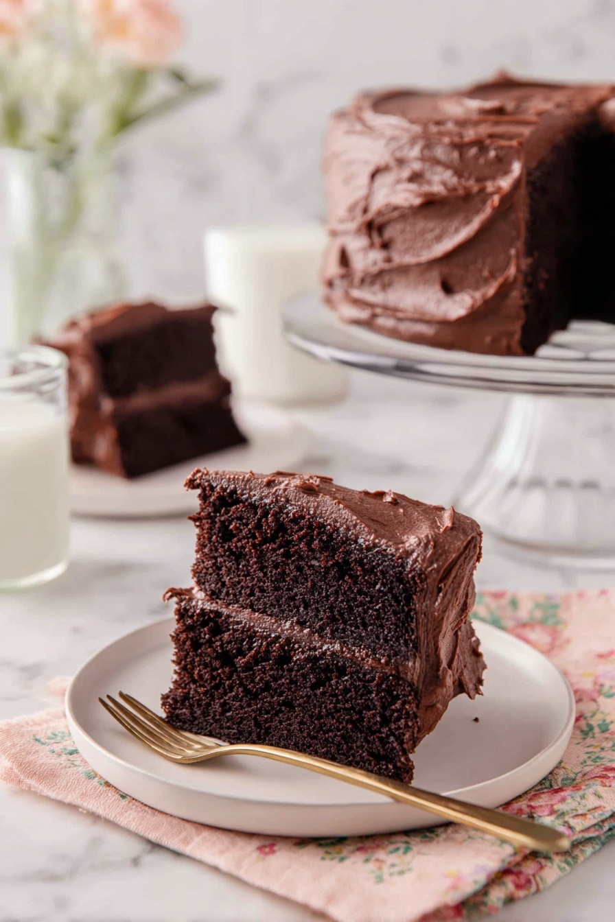 A slice of two-layer chocolate cake with dark, rich cake layers and thick, smooth chocolate frosting both between the layers and on top, presented on a white plate. The frosting on top has a slightly textured, creamy finish with gentle swirls. In the background, there is a full chocolate cake with the same thick frosting on a clear glass cake stand, and another slice of cake on a white plate. Next to the front plate is a glass of milk and a gold spoon resting on a fabric napkin with a soft floral pattern, all set on a white marbled surface. photo taken with an iphone --ar 2:3 --v 7 - Decadent Chocolate Cake, Chocolate Cake Recipe, Moist Chocolate Cake, Rich Chocolate Cake, Easy Chocolate Cake