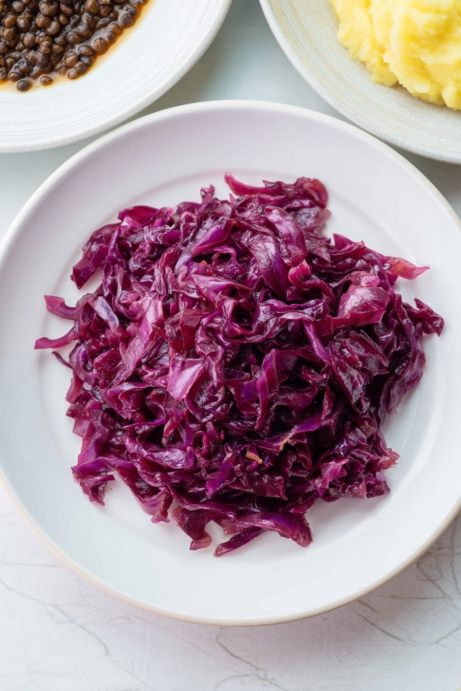 A white plate filled with a generous serving of cooked red cabbage, showing deep purple and reddish hues with a slightly glossy, soft texture. The cabbage strands are layered loosely and appear tender, piled take up most of the plate’s center. The plate sits on a white marbled surface, with parts of two other white plates visible at the top edges, containing dark lentils in brown sauce and creamy mashed potatoes in light yellow color. Photo taken with an iphone --ar 2:3 --v 7 - Braised Red Cabbage, Red Cabbage Side Dish, How to Make Braised Red Cabbage, Red Cabbage Recipes, Easy Braised Red Cabbage