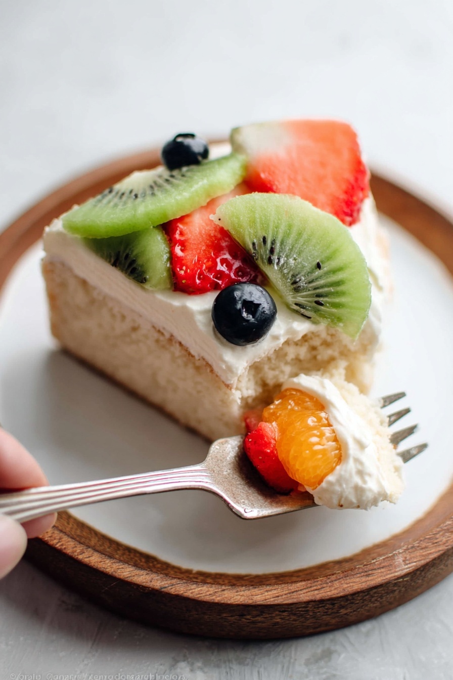 A piece of cake on a round white plate with a white marbled background, showing three layers: the bottom layer is light beige cake with a soft texture, the middle layer is smooth white cream spread evenly on top, and the top layer is fresh fruit pieces arranged closely, including green kiwi slices with visible seeds, red strawberry slices, and small dark blue blueberries. A silver fork on the plate holds a small bite of the cake with cream and a piece of orange fruit, and a woman's hand is about to hold it. Photo taken with an iphone --ar 2:3 --v 7 - Fruit Pizza with Cream Cheese Frosting, fruit pizza recipe, easy fruit pizza, homemade fruit dessert, festive fruit pizza