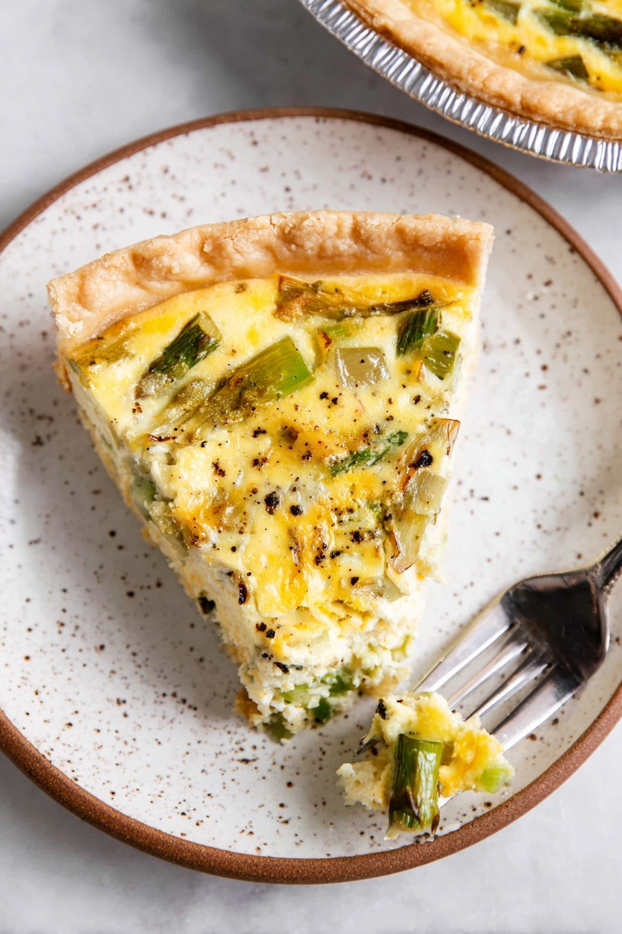 A single slice of quiche sits on a white speckled plate with a brown rim, showing three distinct layers: a golden, thick crust forming the base and edge, a creamy pale yellow egg mixture studded with green vegetables like chopped asparagus and leeks spread evenly in the middle, and a top layer of slightly browned eggs with visible bits of black pepper sprinkled throughout. A silver fork holds a small bite of the quiche near the bottom right of the plate. Part of the whole quiche in a silver pie tin is slightly visible in the top right corner on a white marbled surface. Photo taken with an iphone --ar 2:3 --v 7 - Asparagus and Leek Quiche with Gruyère, asparagus leek quiche, savory vegetable quiche, brunch recipe with asparagus, cheesy leek tart