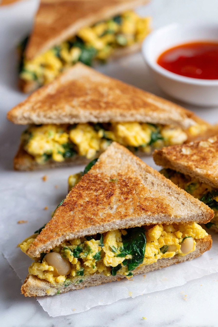 The image shows several triangular sandwiches with a light brown toasted crust. Each sandwich has two layers of golden brown crispy bread, filled with yellow scrambled eggs mixed with green spinach leaves and white beans. The sandwiches are placed on white parchment paper over a white marbled surface. In the background, there is a small white bowl with bright red dipping sauce. The whole setting is simple and clean with a focus on the texture and colors of the sandwiches. photo taken with an iphone --ar 2:3 --v 7 - Healthy Spinach Egg Quesadilla, nutritious breakfast ideas, quick breakfast recipes, healthy egg breakfast, spinach and cheese quesadilla